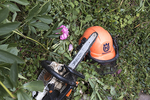 Eine Kettensäge und ein Helm liegen im Gras.