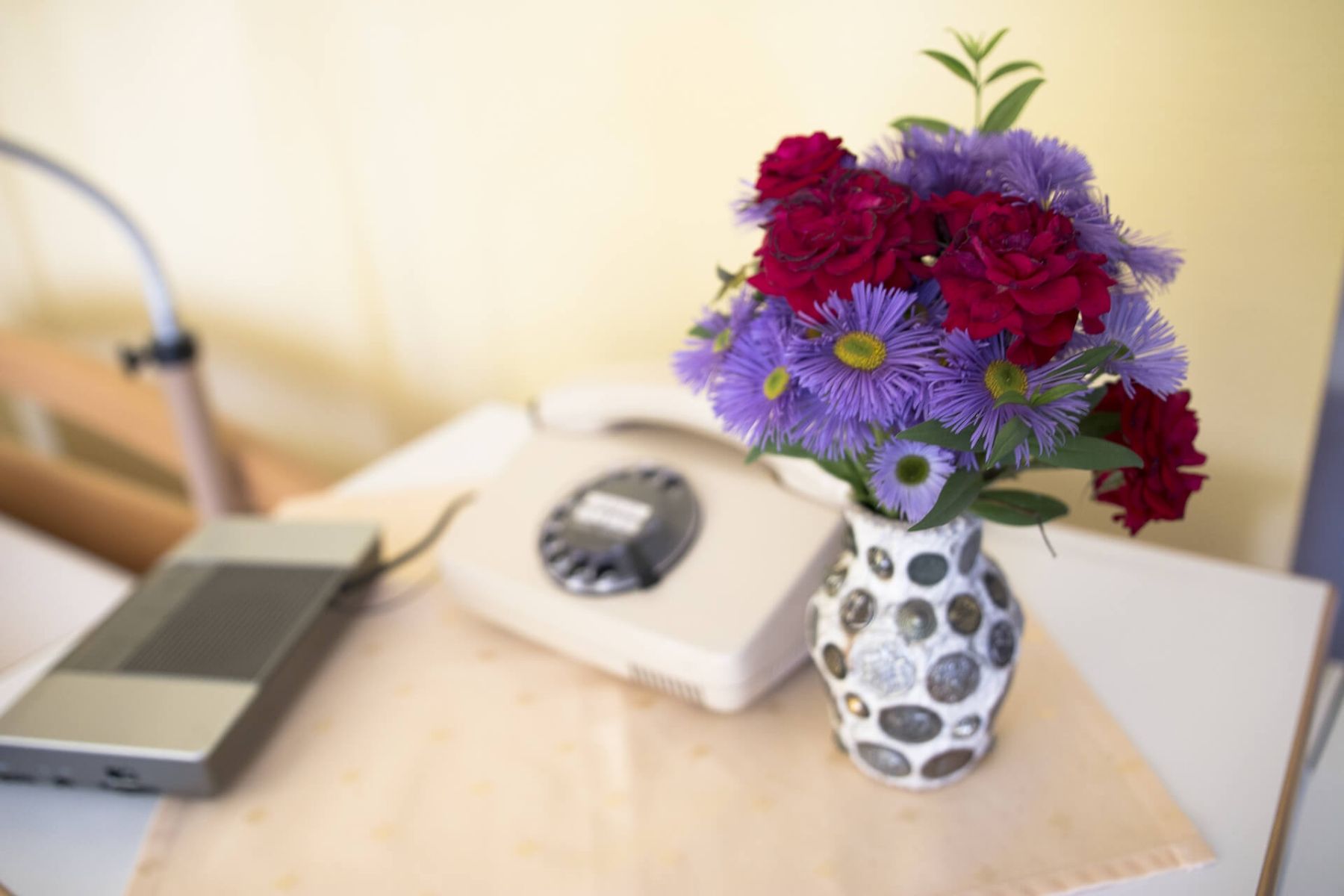 Blumenvase mit frischen Blumen neben einem alten Telefon auf einem Nachttisch.