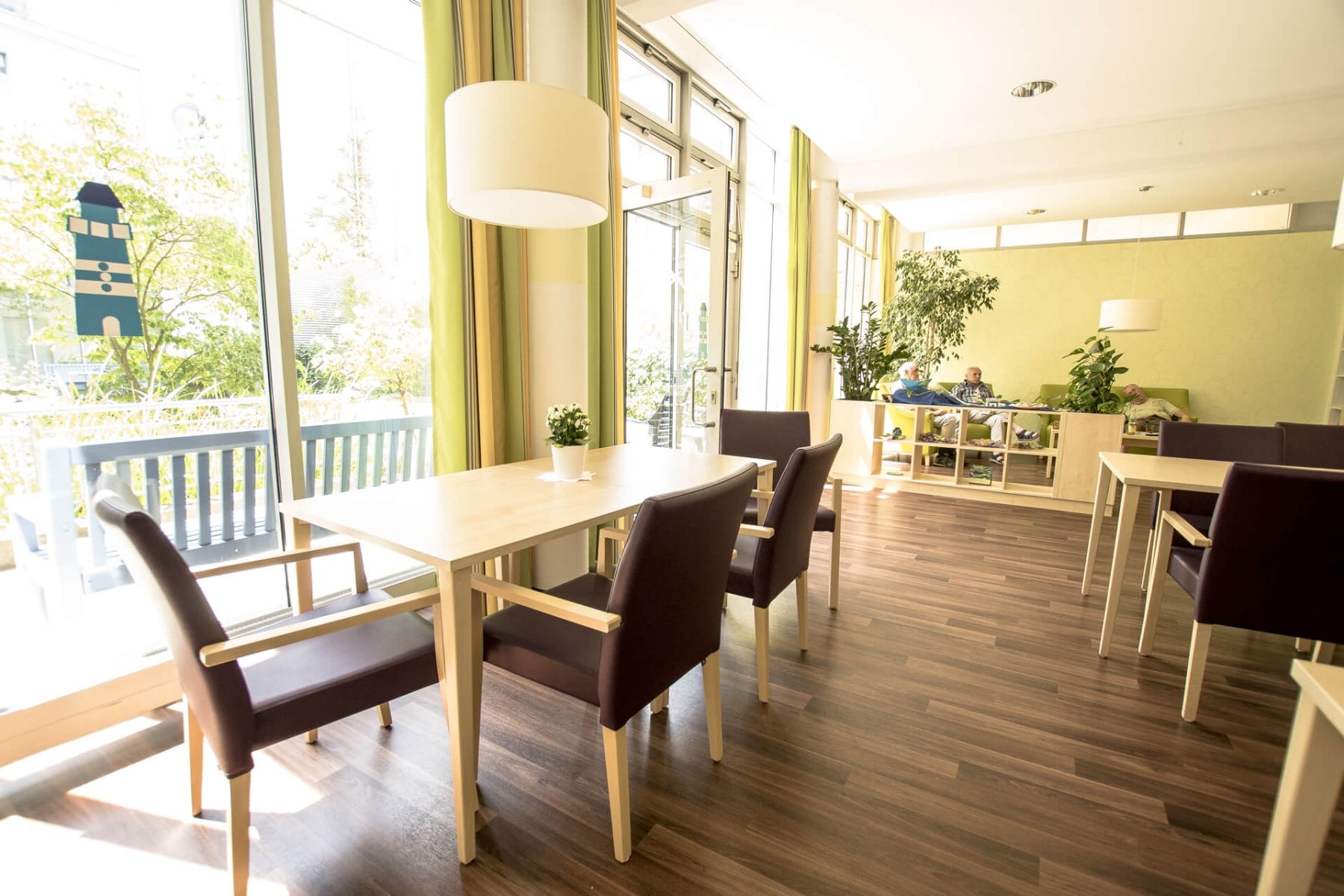 Heller Gemeinschaftsraum mit Esstischen, großen Fenstern und gemütlicher Sitzecke.