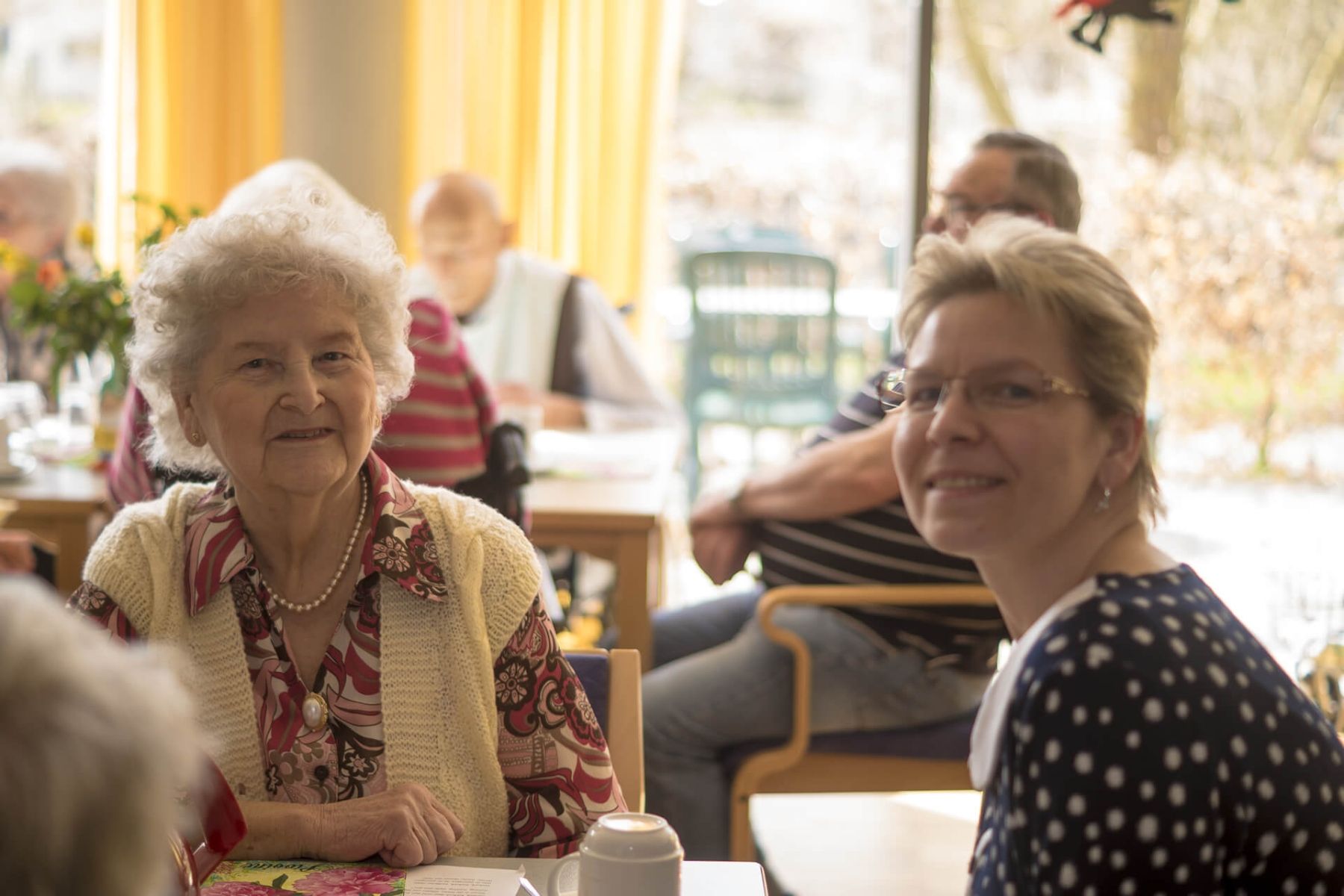 Eine ältere Dame und eine Betreuerin lächeln gemeinsam in die Kamera.