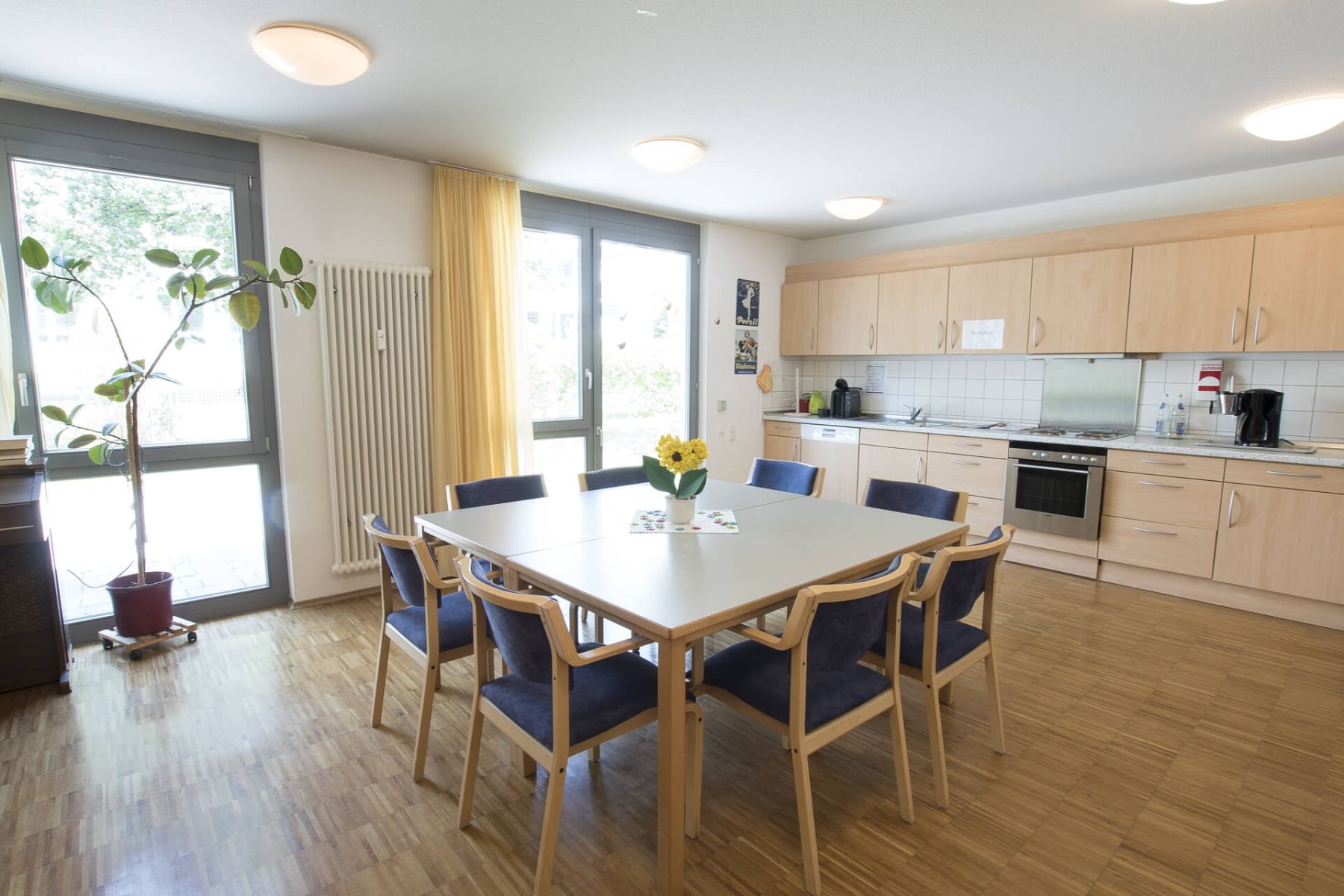 Helle Gemeinschaftsküche mit großem Esstisch und acht Stühlen.