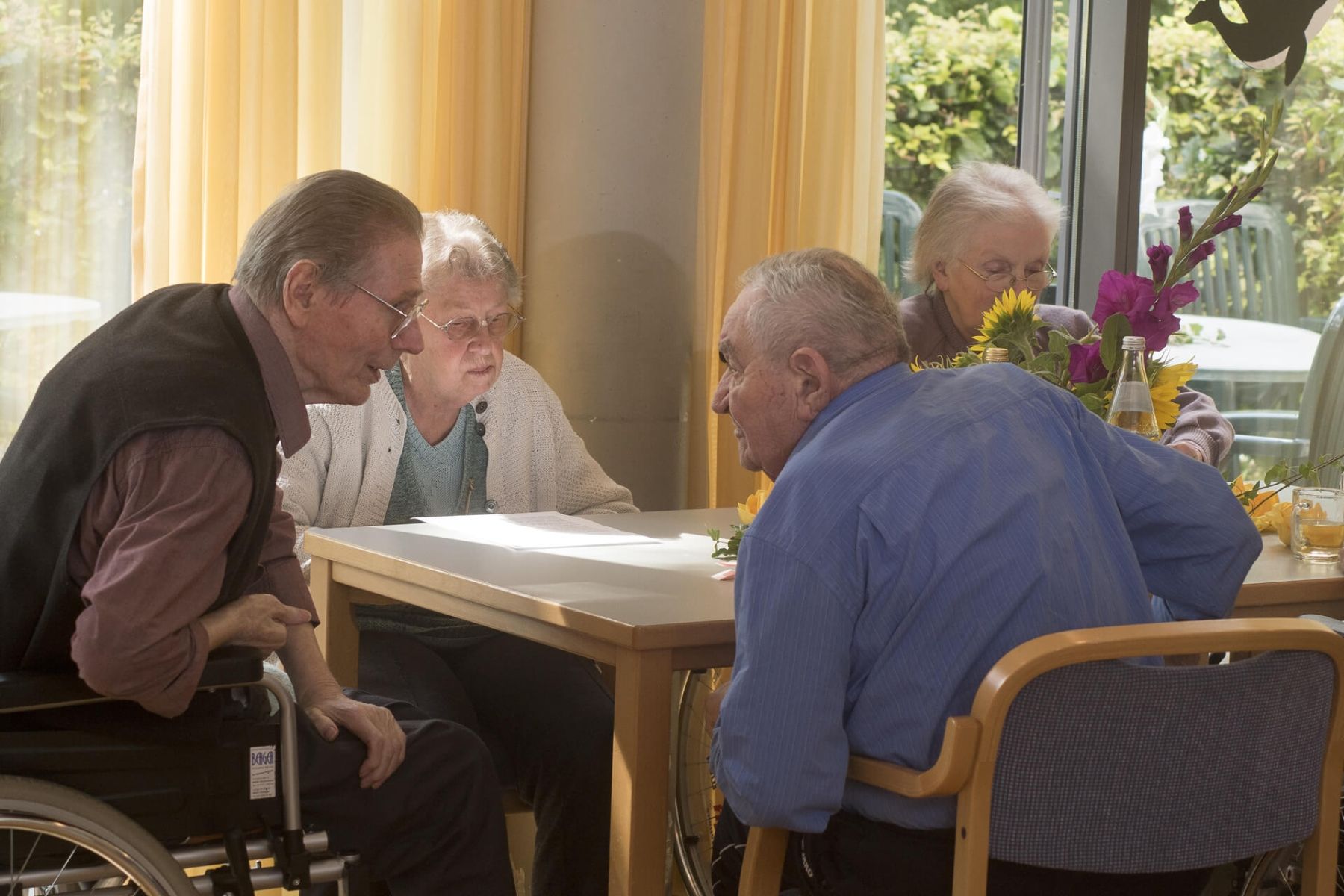 Vier Senioren sitzen zusammen an einem Tisch und unterhalten sich.