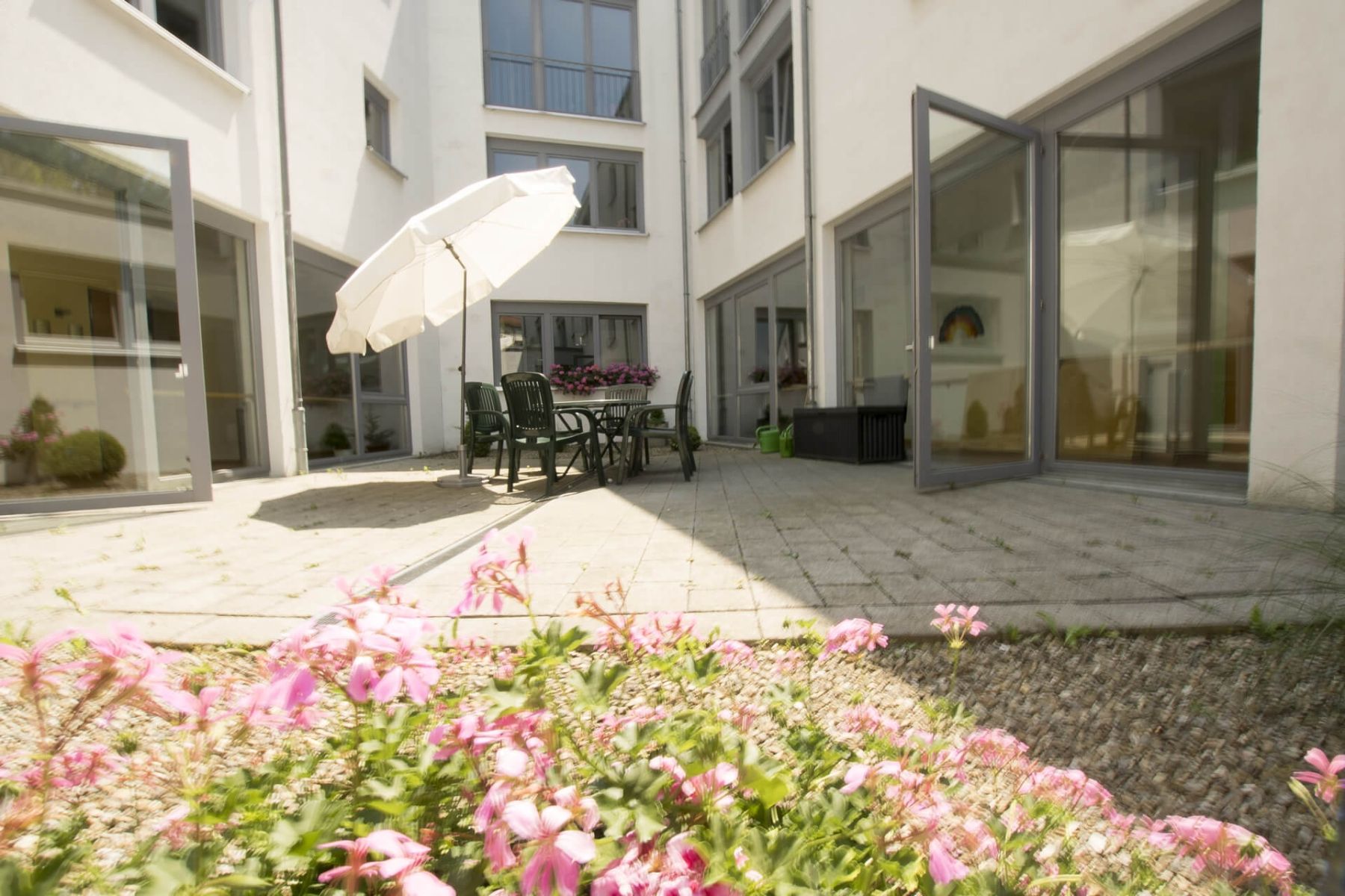 Ein sonniger Innenhof mit Sitzgelegenheiten und Blumen lädt zum Verweilen ein.